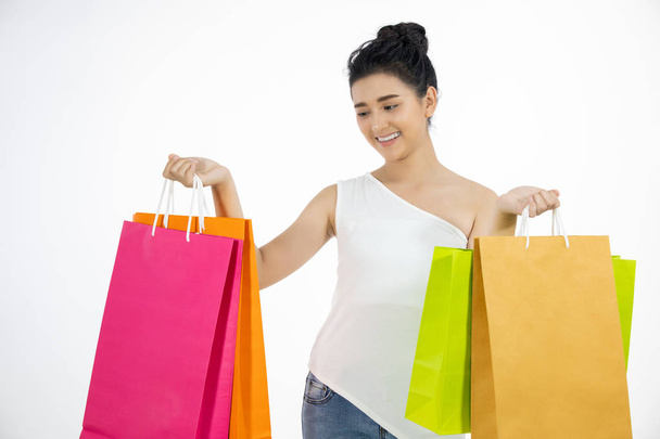 привлекательная брюнетка азиатская женщина держит улыбающиеся и покупки сумки изолированы на белом фоне
 - Фото, изображение