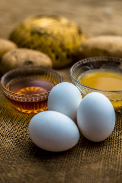 χυμό πατάτας καλά αναμεμειγμένο με μέλι και κρόκους αυγών σε μπολ κατά μήκος ωμό πατάτες και αυγά σε ξύλινη επιφάνεια, έννοια του σπιτικά όλο και πιο στρογγυλεμένο θεραπεία τριχοφυΐα που θα λειτουργήσει ως ένα μαλακτικό, καθώς και ανάπτυξης τριχοφυΐα  - Φωτογραφία, εικόνα