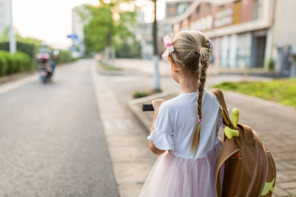 Kid girl pupil from behind walking back to home after learning study school alone with schoolbag, preschool and kindergarten education concept. First day of autumn - 写真・画像