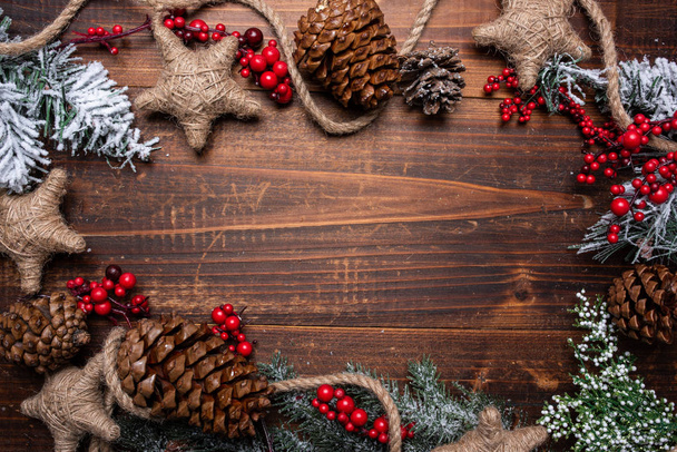 Christmas decorations on a brown wood background with copy space. Pine cones, garland, berries and pine branches - Zdjęcie, obraz