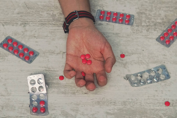 samobójstwo, depresja i koncepcja przedawkowania martwy człowiek z butelką alkoholu i pigułki leżącego na stole w nocy, czerwone tabletki w ręku młodego mężczyzny - Zdjęcie, obraz
