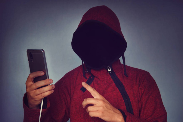 Faceless unrecognizable hooded person using mobile phone, identity theft and technology crime concept, selective focus on body. hacking a smartphone. identity theft. - Photo, Image
