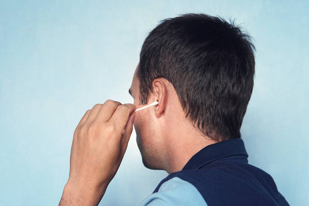 Mann reinigt Ohr mit Wattestäbchen auf blauem Hintergrund. - Foto, Bild