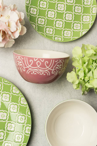 Platón hondo de ceramica rosada con grabados blancos acompaado de platos pandos verdes y flores artificiales
 - Foto, Imagen