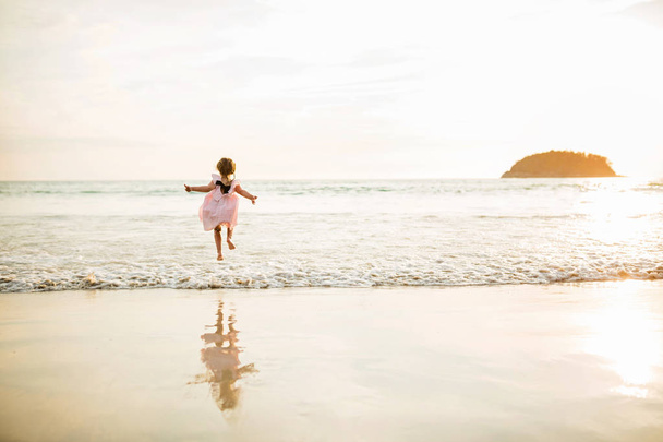 Cute little girl jumping on the beach. Sunset time. Kid having fun in holiday vacation with back sun light - Youth, lifestyle, travel and happiness concept - Foto, Bild