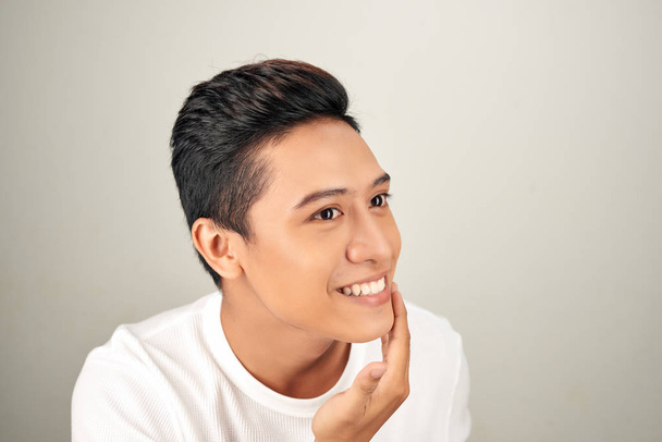 Retrato de un joven asiático guapo sin camisa revisando su cara para el cuidado de la piel y conceptos de belleza sobre fondo blanco
 - Foto, Imagen