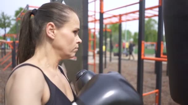 Rostro de mujer boxeadora adulta entrenando con bolsa de boxeo .City park al aire libre. Disparo constante, cámara lenta
 - Metraje, vídeo