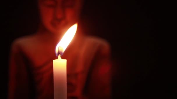 Dmuchanie białą świeczkę w ciemności i posąg Buddy twarz na czarnym tle - Materiał filmowy, wideo