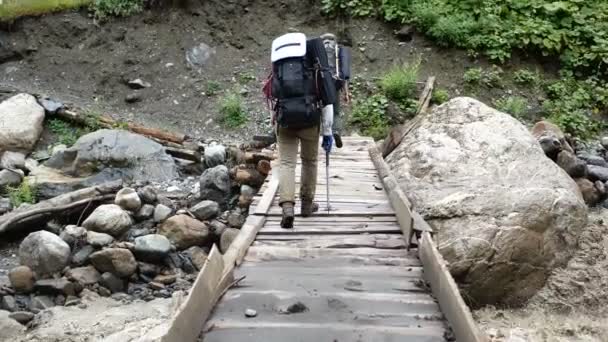 Δύο νεαροί ορειβάτες πηγαίνουν σε μια ξύλινη γέφυρα στα Γεωργιανά Όρη σε αργή κίνηση - Πλάνα, βίντεο
