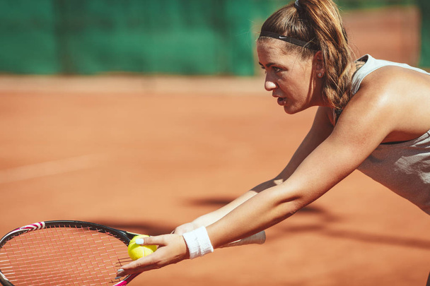 Nuori nainen tennispelaaja palvelee tennisottelun savi kentällä
 - Valokuva, kuva