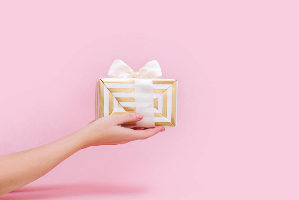 Femmes mains tenant cadeau ou boîte cadeau sur fond rose pastel
. - Photo, image
