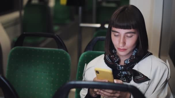 Portrait of young stylish woman browsing on mobile phone in public transport. Young urban professional successful business woman receiving good new. City lights background. - Felvétel, videó