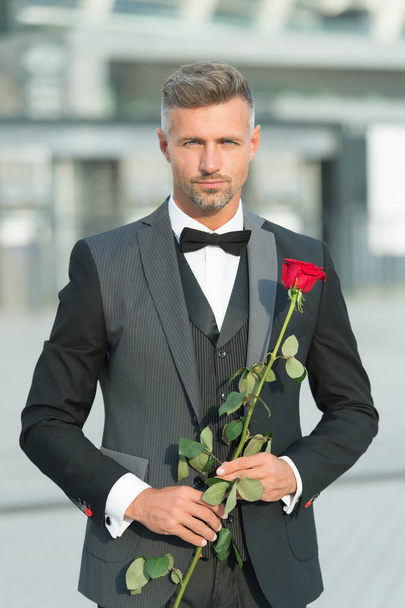 Dating services. How to be romantic. Perfectionist concept. Romantic gentleman. Man mature confident macho with romantic gift. Handsome guy rose flower romantic date. Valentines day and anniversary - Photo, image