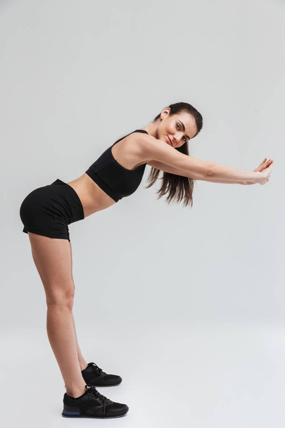 Beautiful young sport fitness woman make exercises isolated over grey wall background. - Фото, изображение