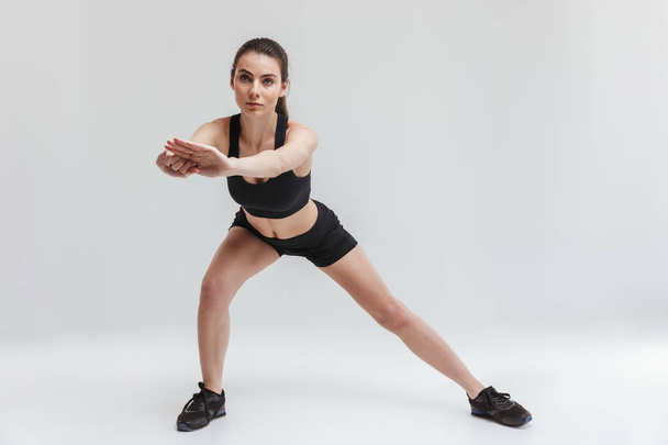 Beautiful young sport fitness woman make exercises isolated over grey wall background. - Zdjęcie, obraz