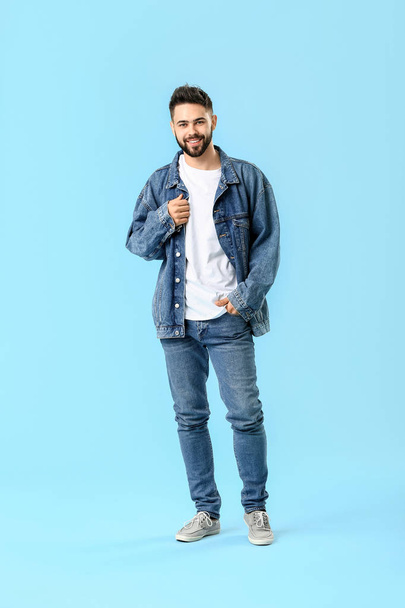Stylish young man in jeans clothes on color background - Foto, afbeelding