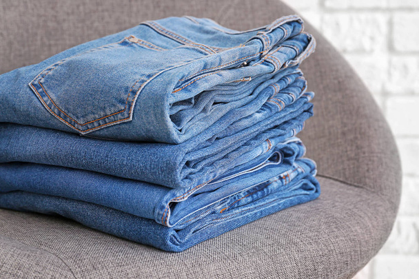 Stack of stylish jeans pants in armchair - Zdjęcie, obraz