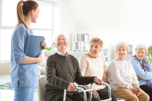 Young caregiver with group of senior people in nursing home - Foto, Imagen