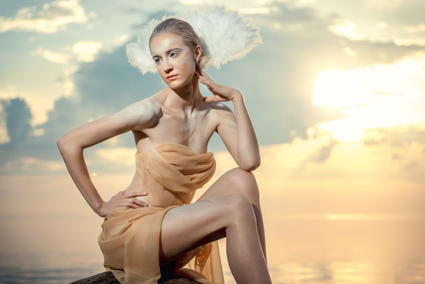 Young beautiful woman as swan posing on the beach at sunset - Фото, зображення
