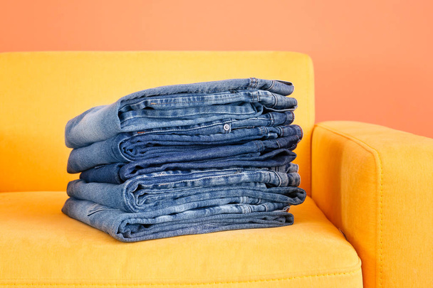Stack of jeans pants in armchair on color background - Photo, Image