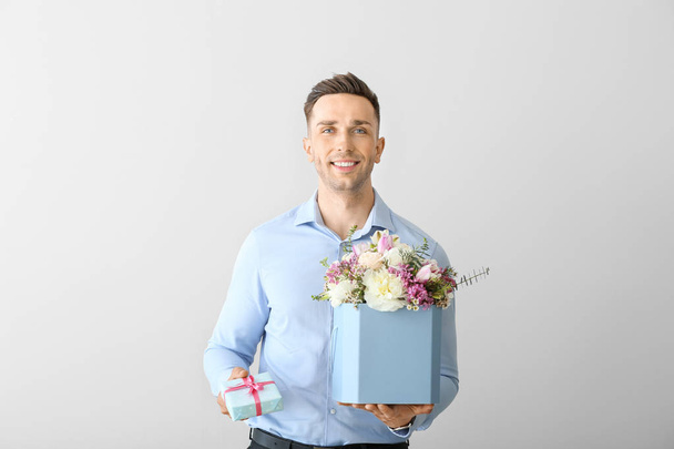 Handsome man with bouquet of beautiful flowers and gift box on light background - Foto, imagen