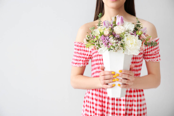 Beautiful young woman with bouquet of flowers on light background - 写真・画像