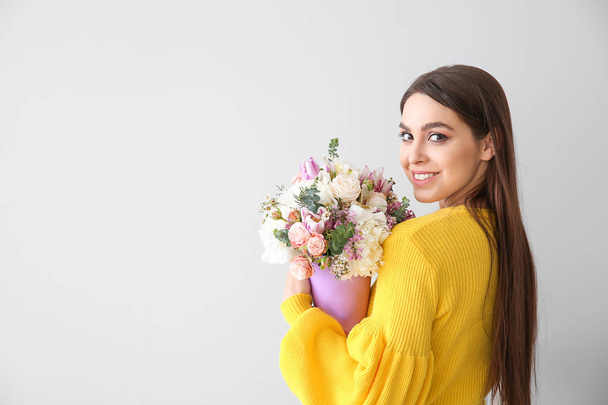 Beautiful young woman with bouquet of flowers on light background - Photo, Image