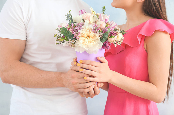 Young couple with bouquet of beautiful flowers on light background, closeup - Φωτογραφία, εικόνα