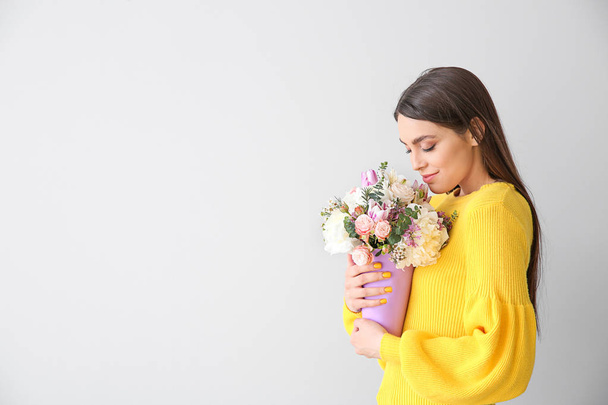 Belle jeune femme avec bouquet de fleurs sur fond clair
 - Photo, image