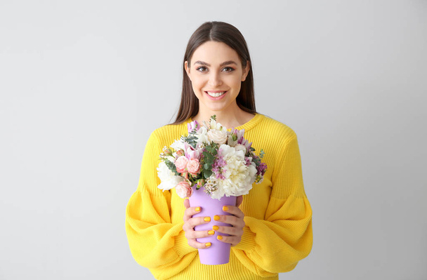 Schöne junge Frau mit Blumenstrauß auf hellem Hintergrund - Foto, Bild