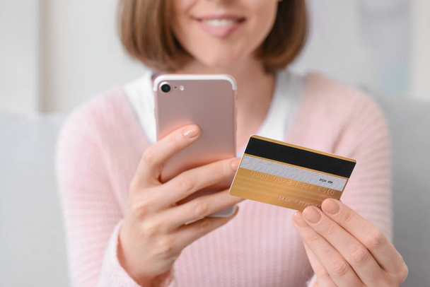 Jonge vrouw met creditcard en mobiele telefoon winkelen online thuis, close-up - Foto, afbeelding