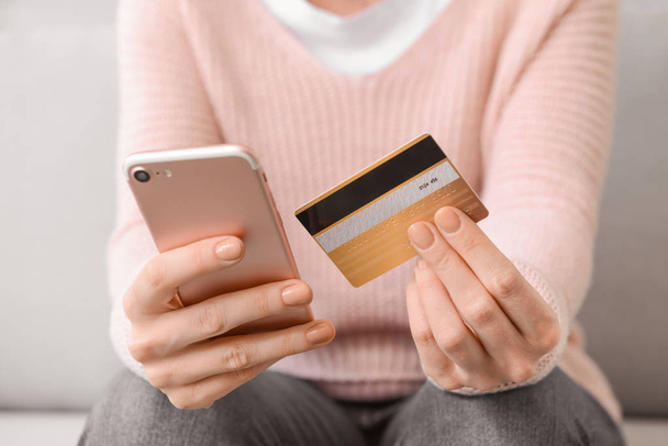 Young woman with credit card and mobile phone shopping online at home, closeup - Fotó, kép
