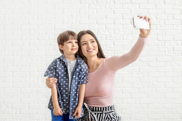 Happy mother and son taking selfie near white brick wall - Fotoğraf, Görsel