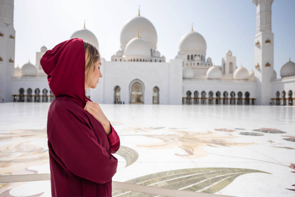 Woman at Abu Dhabi Mosque. Wearing a red Hijab looking at the Sheikh Zayed Grand Mosque in UAE. Sunny day, beautiful architecture views - Foto, afbeelding