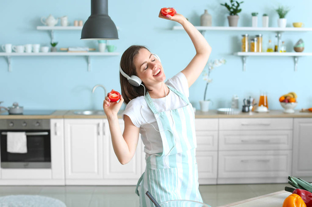Όμορφη νεαρή γυναίκα ακούγοντας μουσική και χορό, ενώ το μαγείρεμα στην κουζίνα - Φωτογραφία, εικόνα