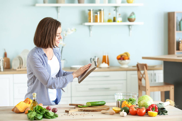 Young woman with recipe book cooking in kitchen - Photo, image