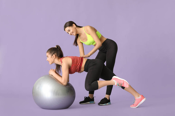 Giovane donna sportiva con fitball fare esercizi sotto la supervisione del suo personal trainer su sfondo di colore
 - Foto, immagini