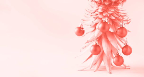 Creative Christmas tree made of pineapple and red bauble on trendy coral color background, copy space. Greeting card, decoration for new year party. Holiday concept. Banner - Фото, изображение