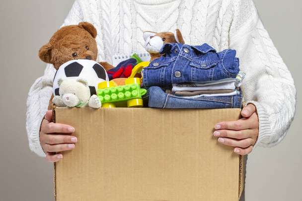 Концепция пожертвований. Женщина держит в руках коробку с одеждой, книгами, школьными принадлежностями и игрушками
 - Фото, изображение