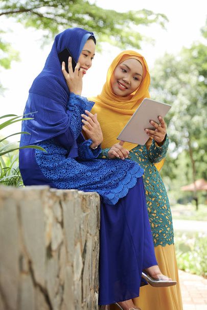 Mosolygó fiatal nő hidzsáb shwing valamit tábla számítógépes barátja beszél telefonon - Fotó, kép