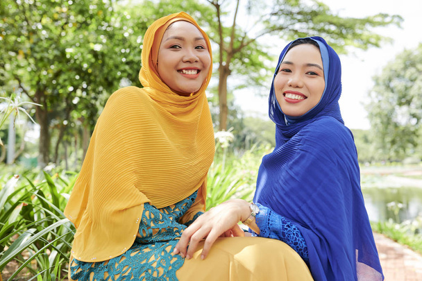 Szczęśliwy młody Muzułmanin kobiet w jasnych hijabs uśmiechnięty i patrząc na kamerę - Zdjęcie, obraz