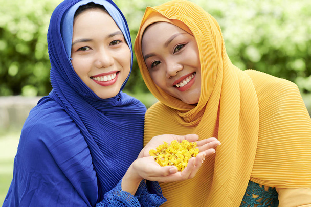 Portré gyönyörű fiatal vietnami nők hijabs mutató maroknyi sárga virágszirmok - Fotó, kép