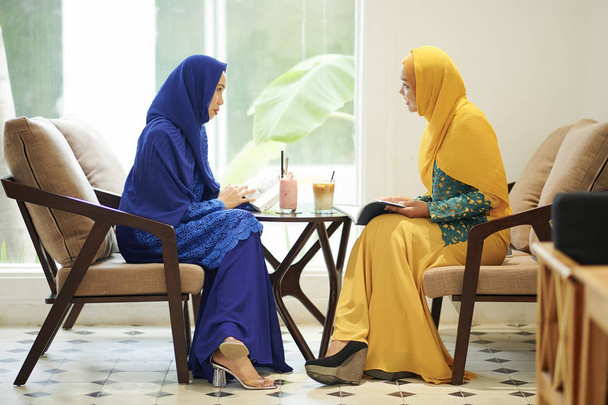 dwie Muzułmańskie kobiety w tradycyjnych sukienkach siedzących przy stole w kawiarni  - Zdjęcie, obraz