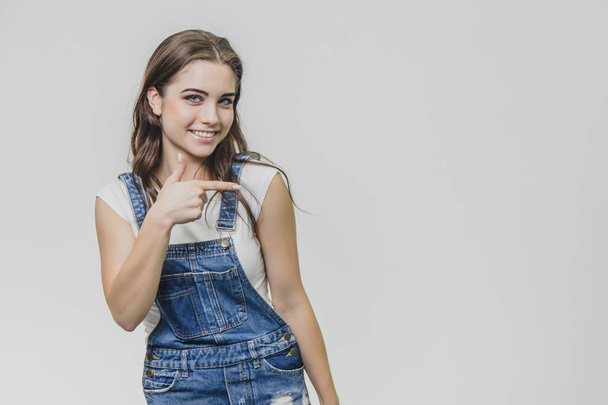 Happy young blond woman in jeans overalls and glasses over grey background - Φωτογραφία, εικόνα