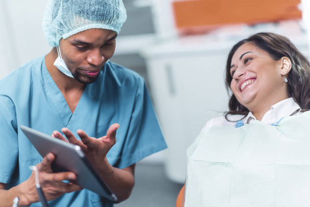 Стоматолог показує своєму пацієнту зображення на електронному пристрої
 - Фото, зображення