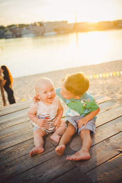 Deux petits garçons assis sur la jetée sur la rive. Concept d'amitié et de fraternité. Journée d'été ensoleillée et joyeuse. Des enfants assis sur la jetée. Deux enfants d'âge différent assis sur une jetée en bois
 - Photo, image