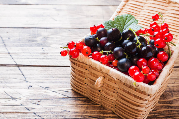 Fresh black and red currant berries in basket on wooden background with copy space. - Фото, зображення