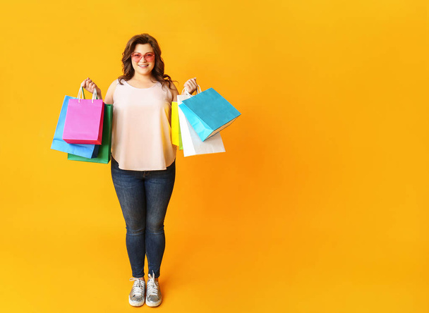 Happy plus size woman with shopping bags on color background - 写真・画像