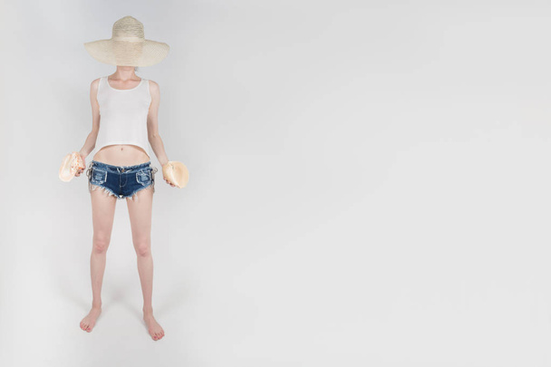 the girl in shorts and hat covering her face staying and holding the clamshells on white background isolated - Photo, image