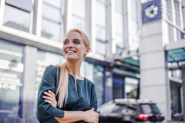 Beautiful young woman, business worker, looking away with smile and happy face. Confident and successful professional over grey urban office building. Image for advertising - Photo, Image